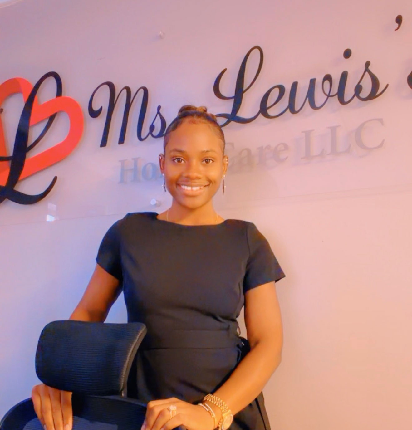 Special Lewis, MBA, posing at her desk. The logo is printed on a lucite plaque, five feet wide, and mounted high on the wall behind her.